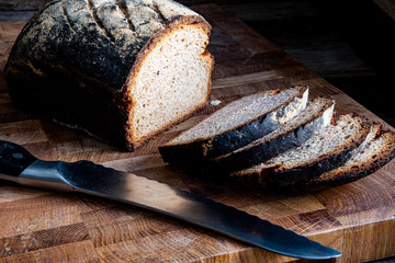Homemade rustic sliced bread on a cutting kitchen board, knife on a wooden background.
