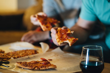 A couple of men and women eat pizza on the sofa in their living room at night while watching a...