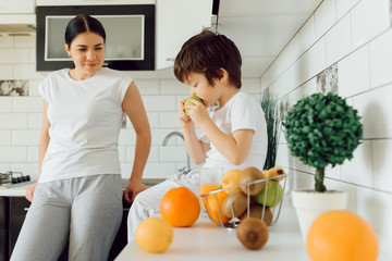 Cute little boy with mother. Family in a kitchen. Mother with son eating fruits.