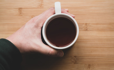 male hand holding cup of coffee on wooden background	