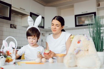 Mother and her son painting Easter eggs. Happy family preparing for Easter day.