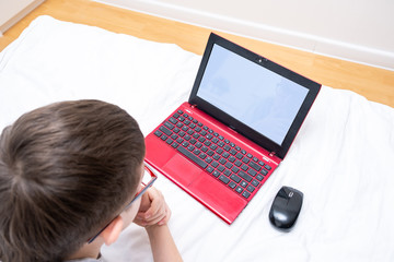 A boy lying in bed with a laptop,distance and e-learning during quarantine and self isolation,...