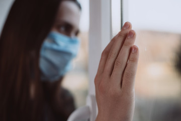 Close up focus on female hand holding on window, thinking about troubles, sad woman in medical sterile face mask thinks about risk of epidemic disease. Self isolation, Home quarantine