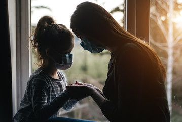 Loving mother embracing upset little daughter with virus mask, young mom comforting, consoling sad preschool girl with health problem. Concept of coronavirus or COVID-19 pandemic disease symptoms