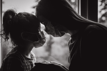 Black and white portrait of loving mother embracing upset little daughter with virus mask, young...