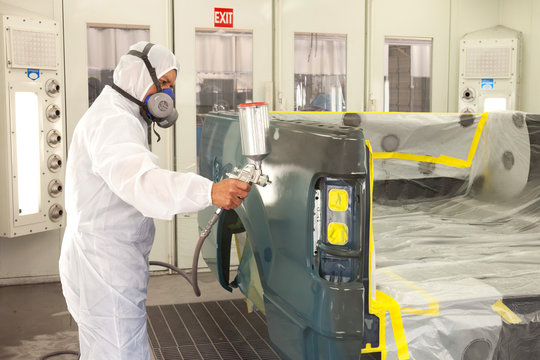 Man in Autobody Shop Painting Car Dressed in White Coveralls with Respirator On