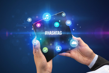 Businessman holding a foldable smartphone with #HASHTAG inscription, social media concept