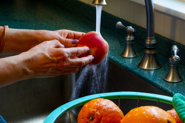 A woman washes fresh apple in a kitchen sink