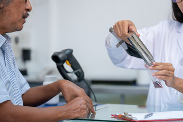 Fototapeta premium Professional young Asian female pharmacist prepare prescription medicine capsule or supplement to senior man patient in hospital pharmacy drugstore. Medical, pharmaceutical and healthcare concept.