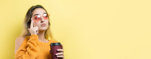 Glamor woman in glasses in an orange sweater with a drink of coffee on a yellow background