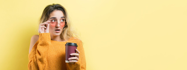 Glamor woman in glasses in an orange sweater with a drink of coffee on a yellow background