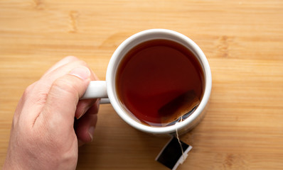 male hand holding cup of coffee on wooden background	