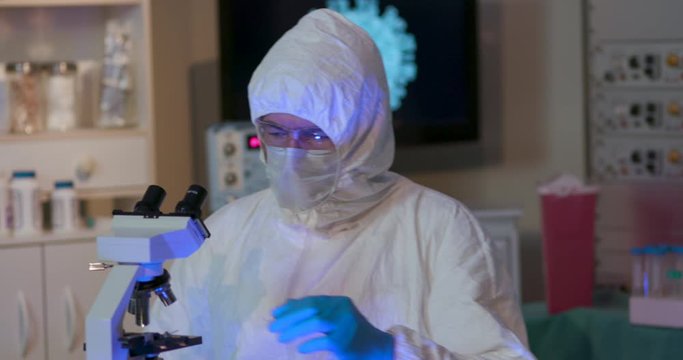 Scene Moves With A Researcher In A Lab With A Graphic Of The Coronavirus COVID19 On A Monitor In The Background Who Returns To His Workstation To Work With A Blood Sample In His Search For A Vaccine.