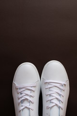 A pair of light sneakers on dark brown background. Top view. Copy space.