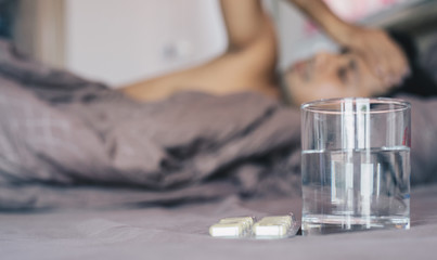 Man sick sleeping in his bed. Focus on glass of water and pills 