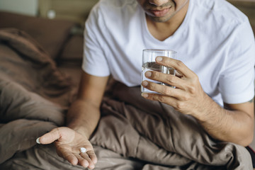 Young man sick taking medicine on the bed, Yong man taking pill and drinking water 