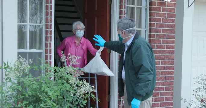 An elderly woman with a walker who is at high risk because of the coronavirus COVID19 gets meals or groceries delivered to her house by a volunteer working with a benevolent organization.
