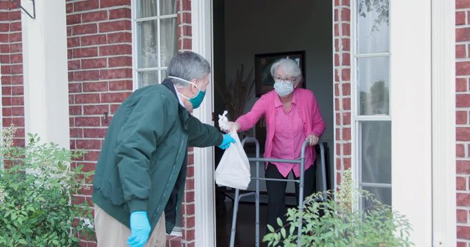 An elderly woman with a walker who is at high risk because of the coronavirus COVID19 gets meals or groceries delivered to her house by a volunteer working with a benevolent organization.