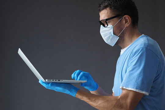 Male Doctor In Medical Mask And Gloves Works In Laptop.