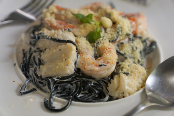 Black spaghetti with shrimps and squid on a white dish