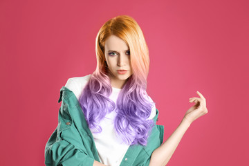 Portrait of young woman with dyed long curly hair on pink background