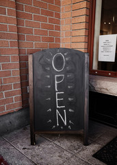 Chalkboard Open sign in front of a store in the daytime.
