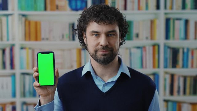 Portrait middle age businessman advertising smartphone vertical mock-up greenscreen chroma key technology devide in the library bookshelves.