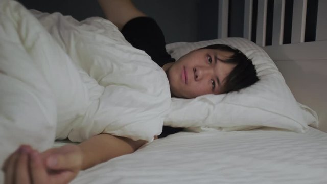 Close up of young asian man tries to sleep and covers his ears with a pillow