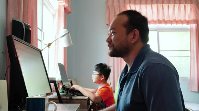 working from home. Asian father using computer in the bedroom with my son In the morning the sunlight sent from the window.