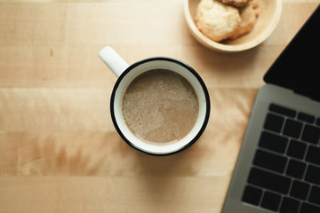 Top view of workspace with laptop and coffee cup on wooden desk.