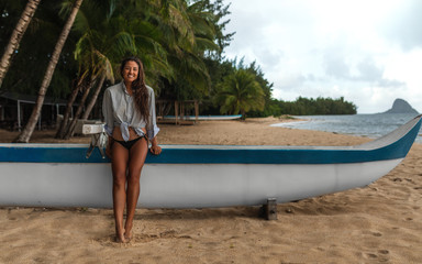 Obraz premium Happy attractive Hawaiian girl seating on canoe on the beach with palm trees and ocean 