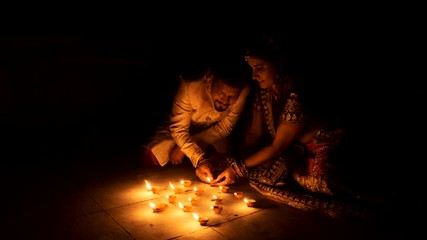 Beautiful Indian Gujarati couple in Indian traditional dress lightening Diwali diya/lamps sitting on the floor in darkness on Diwali evening. Indian lifestyle and Diwali celebration