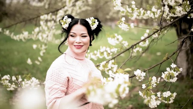 Asian woman in pink sweater in blossoming garden