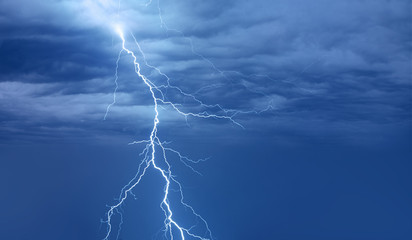 Lightning strikes between blue stormy clouds.