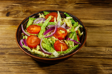 Healthy salad with savoy cabbage, cherry tomato, red onion and olive oil on wooden table