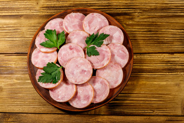 Ham sausage on a plate on wooden table. Top view