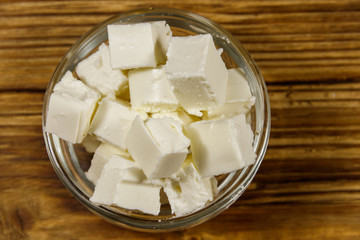 Feta cheese cubes in glass bowl on a wooden table. Top view