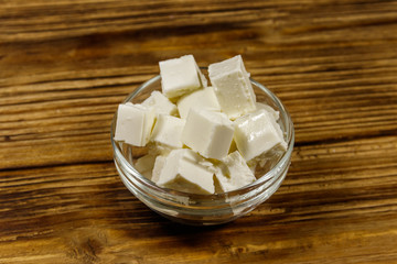 Feta cheese cubes in glass bowl on a wooden table