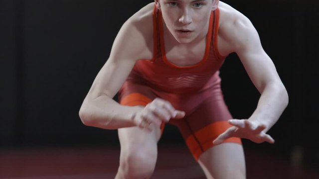Teenage wrestler wearing a red singlet and practice his shadow wrestling drills