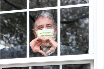 Man wearing mask making heart symbol with hands at the window
