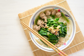 Rice noodles soup with pork meatball and vegetables in a bowl and chopsticks, homemade Asian food, top view