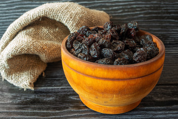Dried prunes in wooden bowl on dark background, rustic