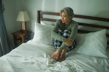 attractive middle aged woman with grey hair sad and depressed in bed feeling scared and lonely...