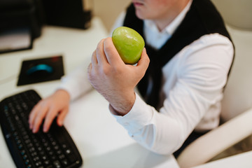
Young caucasian businessman eating apple in office. Desk, man and fruit
