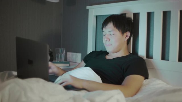 Young asian Man Using A Laptop Late At Night In Bed