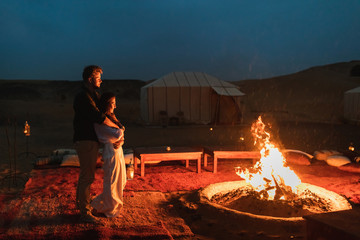 Couple hug in love near big campfire. Romantic night in glamping desert camp in Sahara, Morocco....