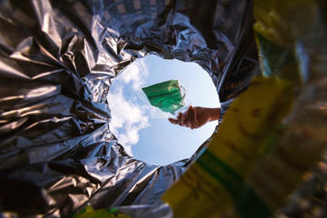 Face mask pack in zip lock before throw into the trash. With a worm view from the inside of the trash bin.