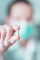 Doctor with medical mask holding white pill. Close up