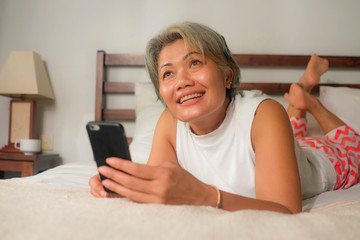 home lifestyle portrait of attractive and happy middle aged woman on her 50s using internet mobile phone in bed relaxed and cheerful online dating or enjoying social media app