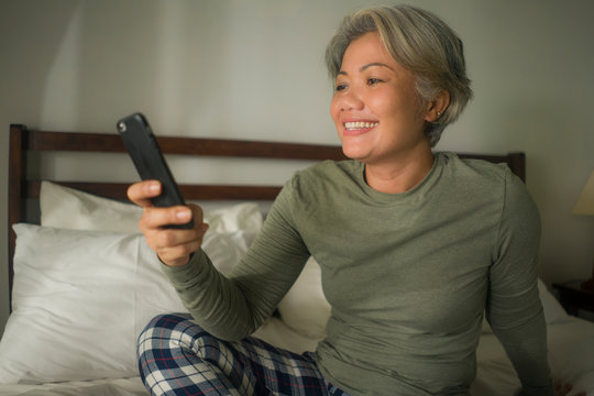 Attractive And Happy Middle Aged Woman On Her 50s Using Internet Mobile Phone In Bed Relaxed And Cheerful Online Dating Or Enjoying Social Media App